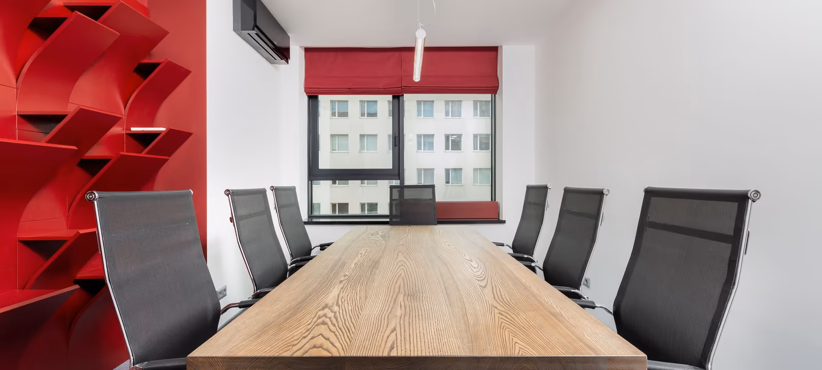 A conference room with chairs pushed to the table and daylight through a wall of windows