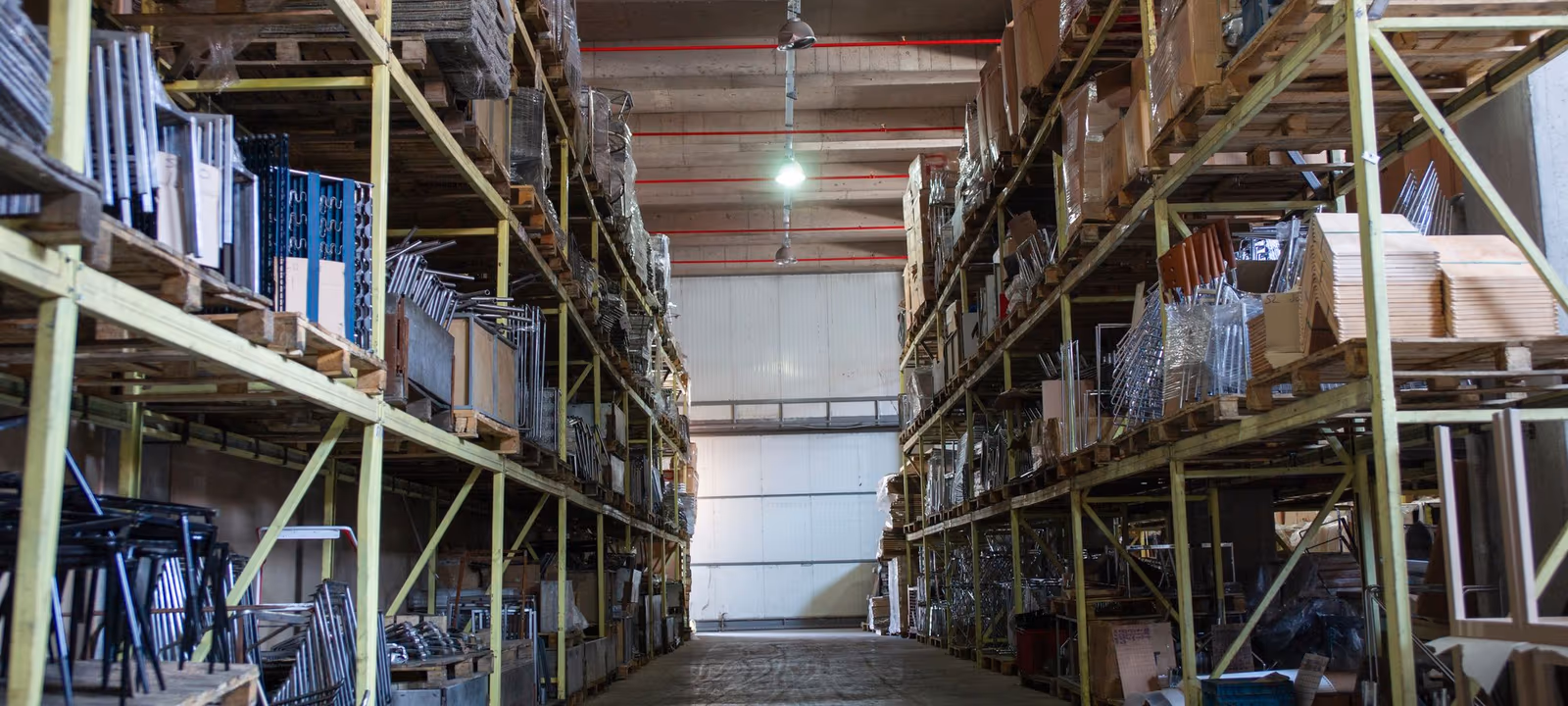 A long receding aisle of industrial racking seen at floor level, pallets stacked to the upper tiers