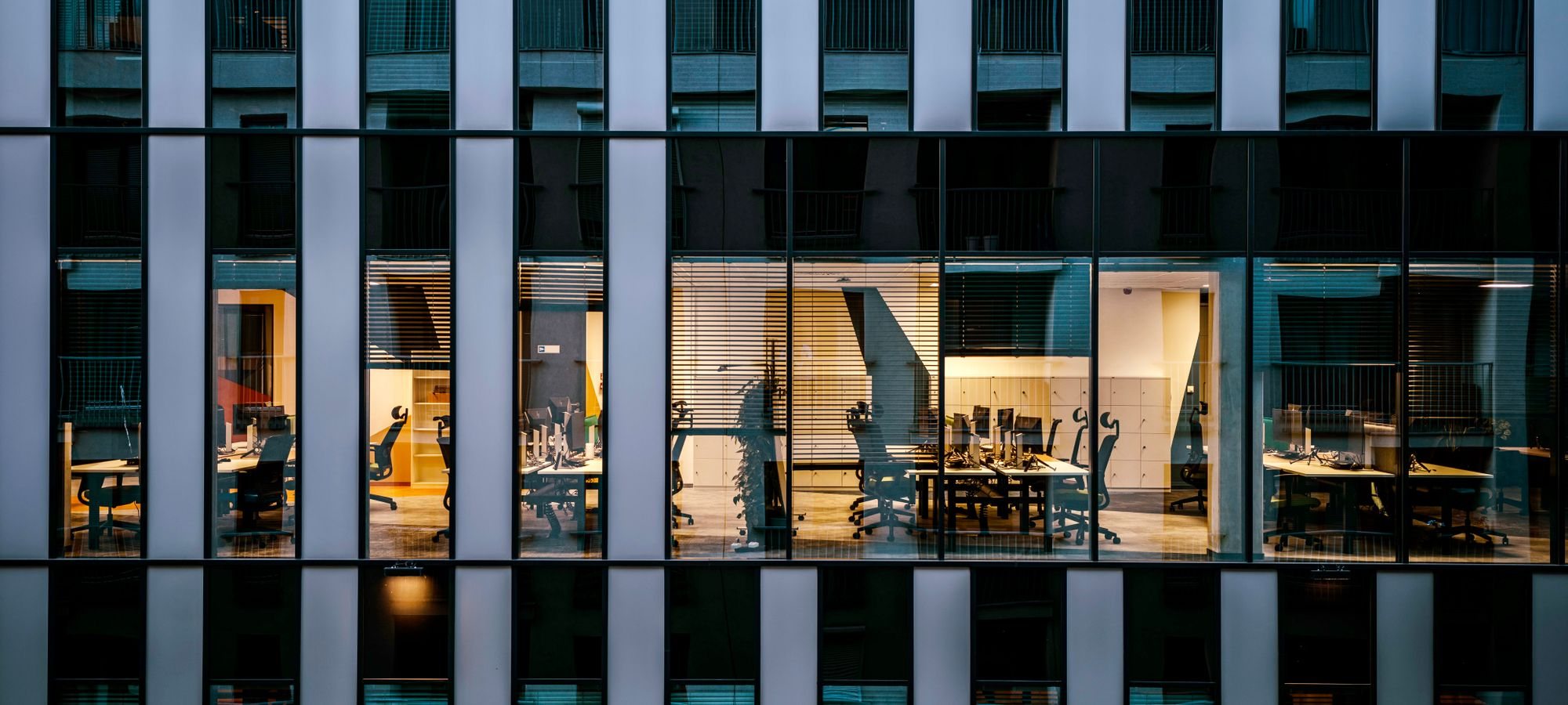 An office floor lit at dusk, seen through the glass facade of a tower