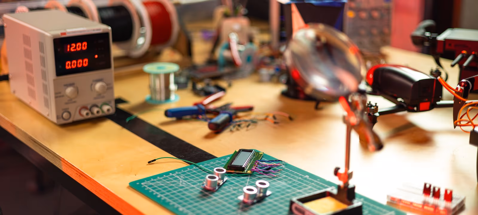 Prototype objects arranged on a workshop table under a bench lamp