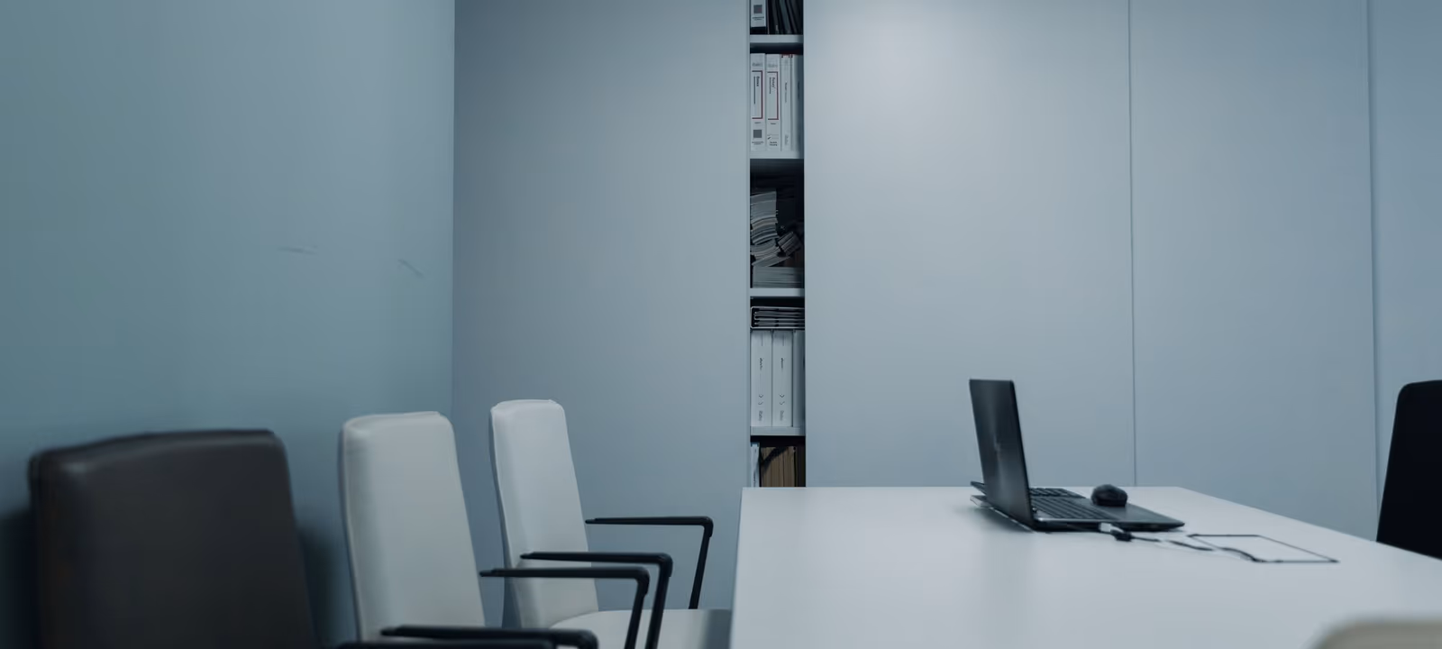 An empty meeting room seen from the doorway, chairs pulled back from a long table under low ceiling lights