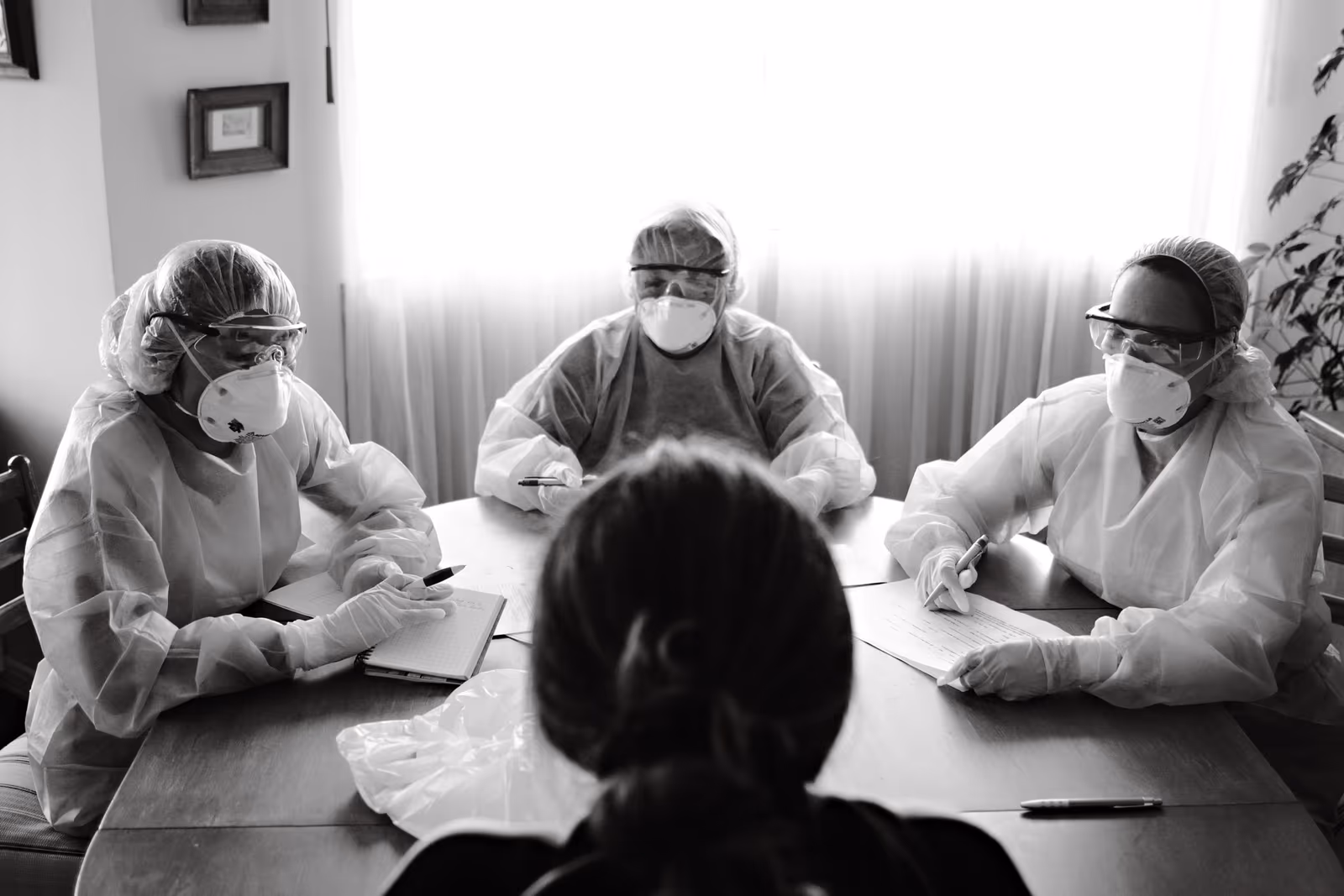 Masked clinicians discussing papers around a table, in black and white